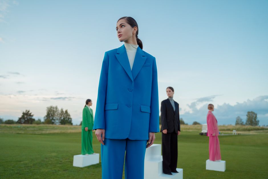 Four women in colourful suits standing on grass under a blue sky, posing artistically.