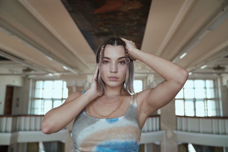 Stylish woman in a tank top poses indoors, showcasing elegant jewelry and modern hairstyle.