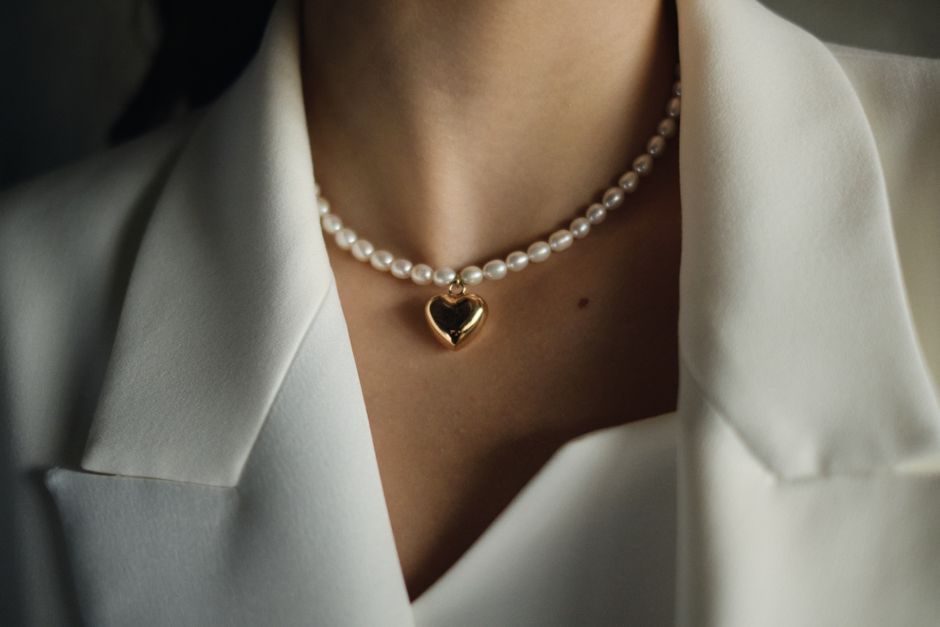 Close-up of a pearl necklace with a gold heart pendant over a white blazer.