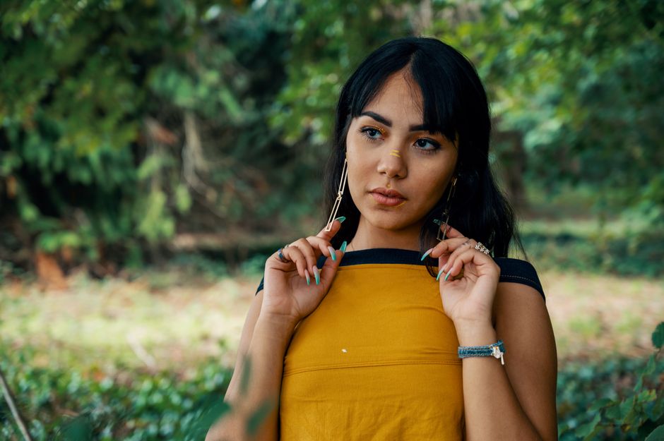 A woman in casual wear poses thoughtfully outdoors, emphasizing her style and natural background.