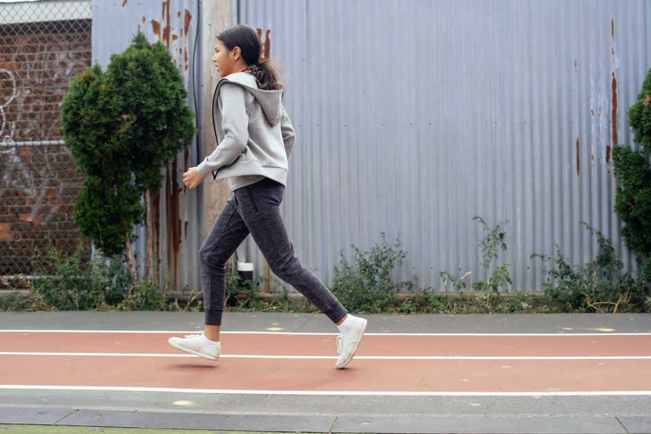 Side view of schoolgirl in sportswear and sneakers jogging on sports ground while spending free time outside