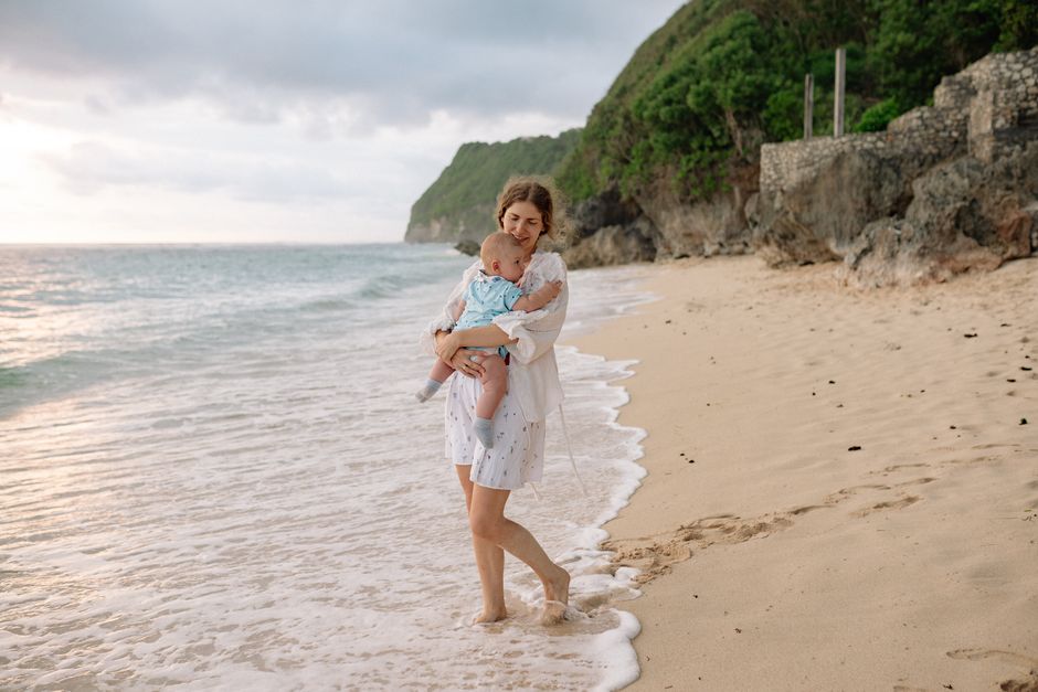 A mother carries her baby along a serene beach, enjoying the summer day.