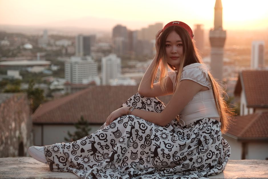 A young woman sitting with an urban backdrop during a stunning sunset.
