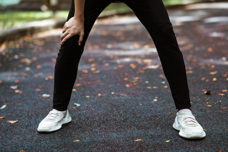 Legs of anonymous runner in white sneakers and black leggings taking breath after running leaning on knee