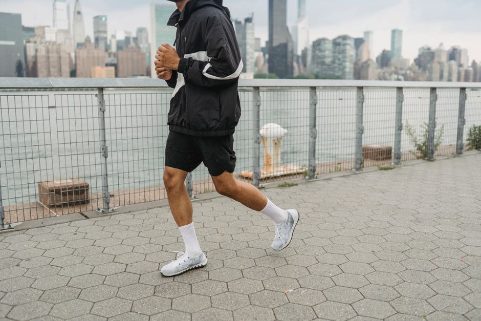 Man jogging along a city waterfront with a skyline view, wearing sportswear.