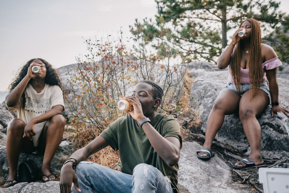 Three friends enjoying drinks outdoors, sitting on rocks and relaxing in nature.
