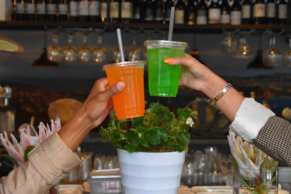 Two hands clinking vibrant drinks in a stylish bar, showcasing a lively atmosphere.