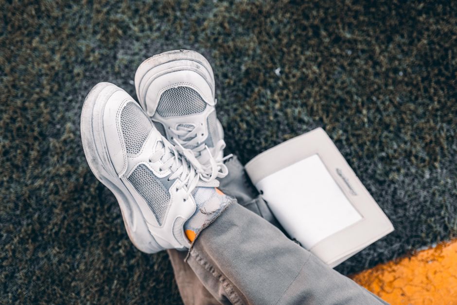 White sneakers casually placed on grass with an open book, conveying a relaxed outdoor vibe.
