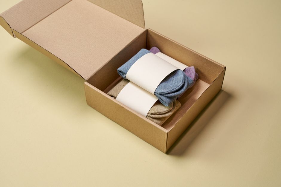 Multicolored socks neatly arranged inside open cardboard packaging on a neutral background.