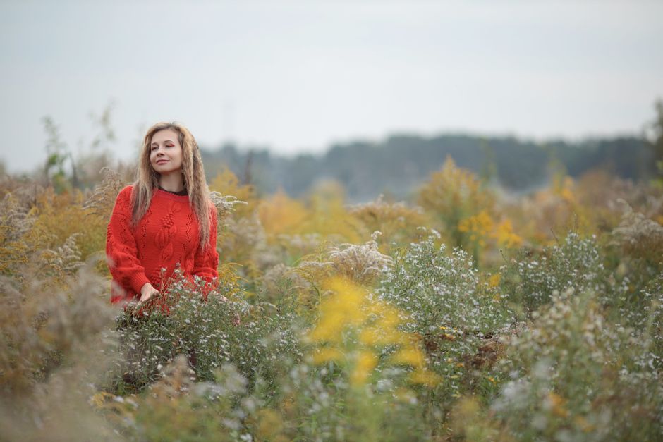A woman in a red sweater enjoying a stroll through a field of wildflowers in autumn.