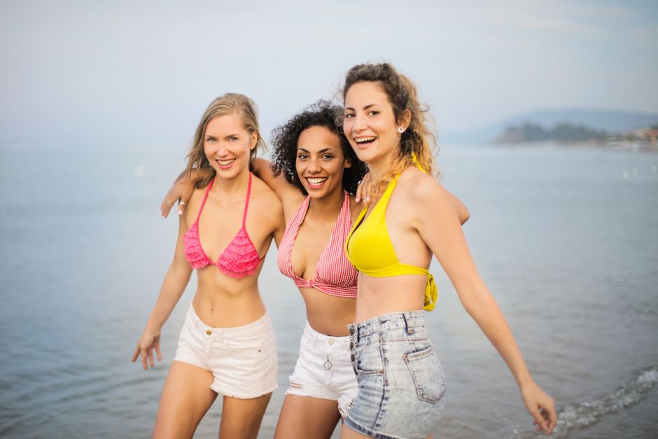 Three friends in bikinis having fun on a sunny beach day, embracing happiness and friendship.