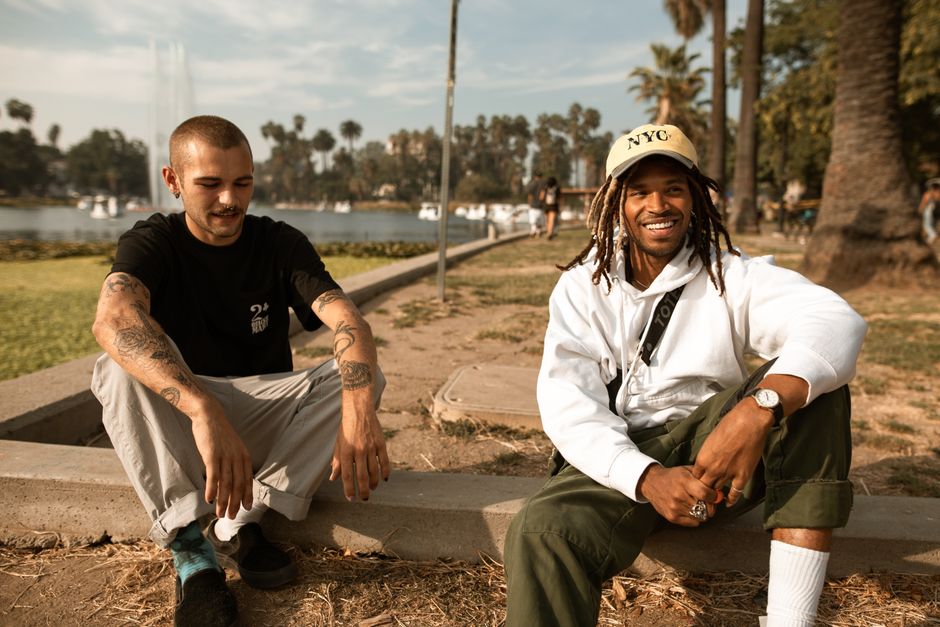 Two friends smile while sitting on a park bench by the lake on a sunny day.
