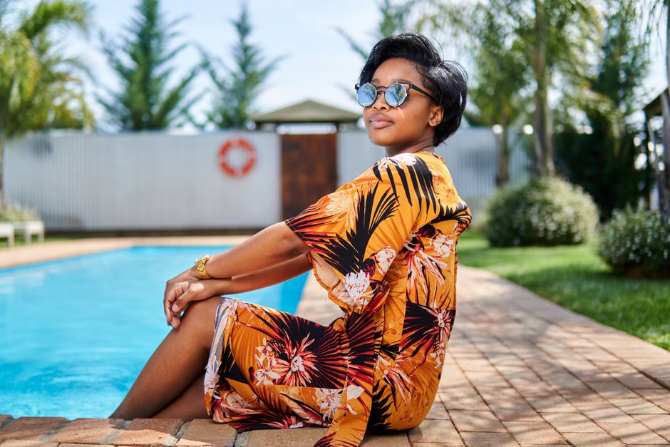 Elegant woman in sunglasses sitting by a pool, enjoying a sunny day outdoors.
