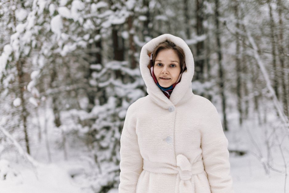 A woman in a white winter coat standing in a snowy forest, exuding warmth and style.