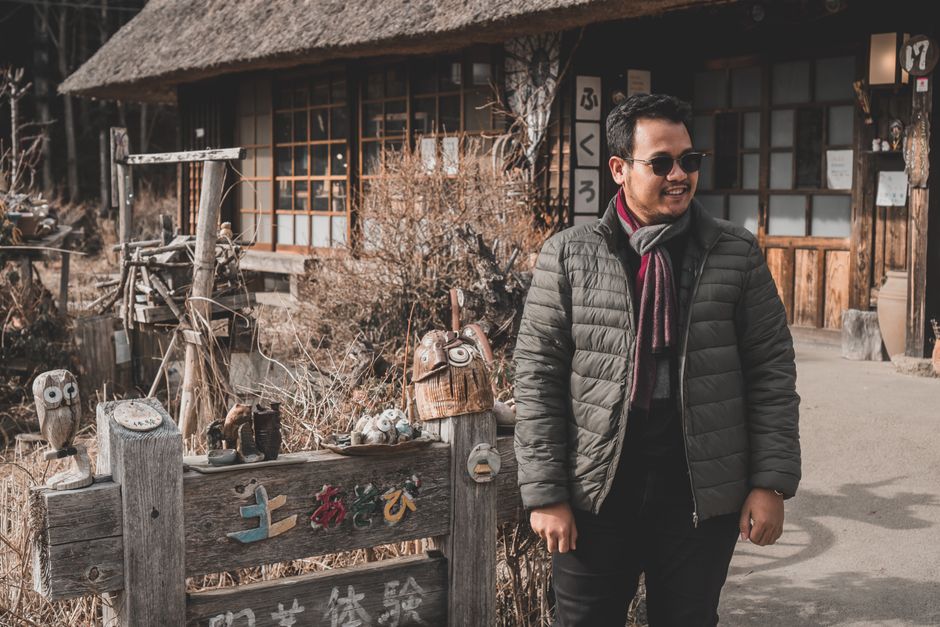 Smiling man in winter jacket with scarf in traditional setting outdoors.