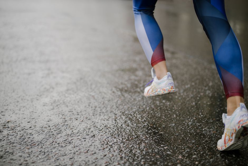 Close-up of a runner's legs wearing colorful shoes on wet pavement.