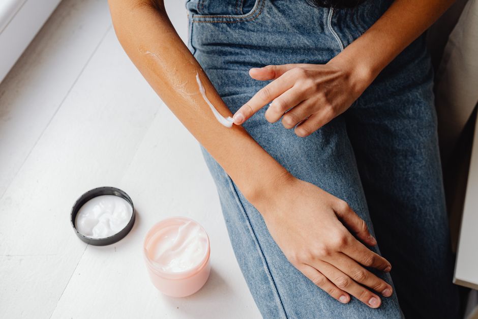 Close-up of a person applying hand cream on their arm, emphasizing skincare and hydration.