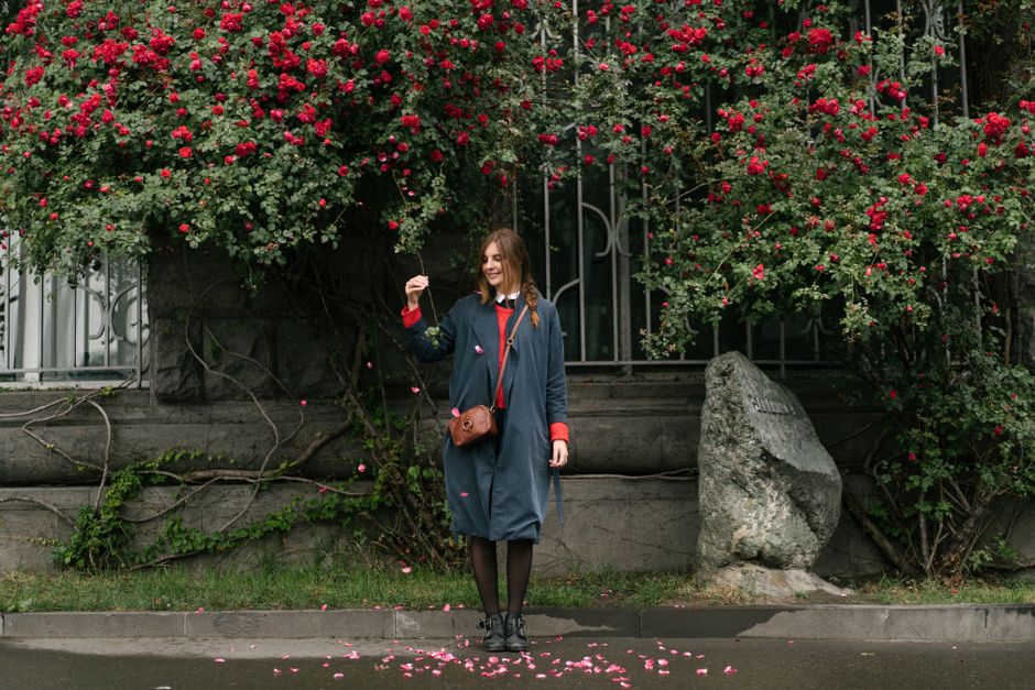 A woman stands happily by a blooming bush on a city sidewalk, capturing spring's charm.