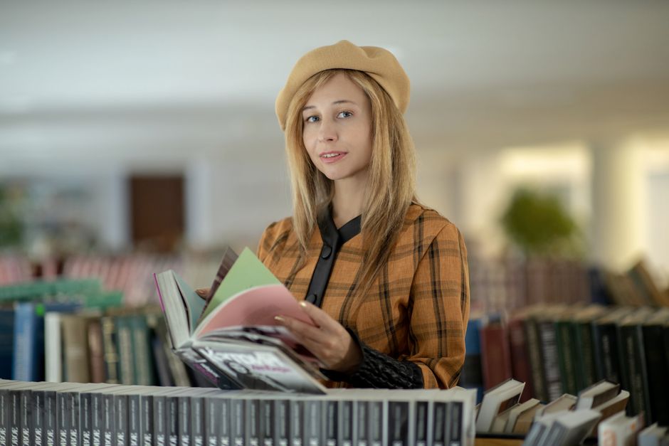 Portrait of a young woman reading a book in a cozy library setting, wearing a beret.