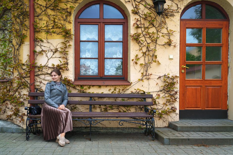 A stylish woman sits on a bench near an ivy-covered wall in Pinsk, Belarus. Elegant and tranquil setting.