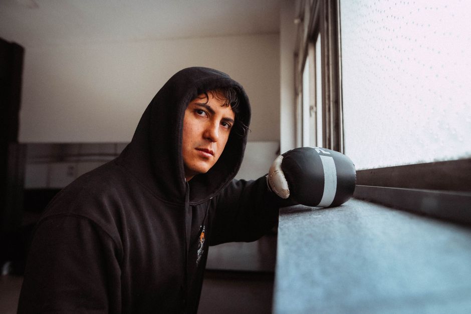 A focused boxer in a hoodie and gloves, training indoors in Buenos Aires, Argentina.