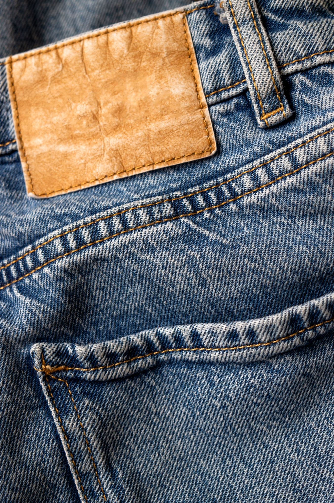 Folded blue denim showing waistband, belt loop, label patch, yoke stitching and back pocket.
