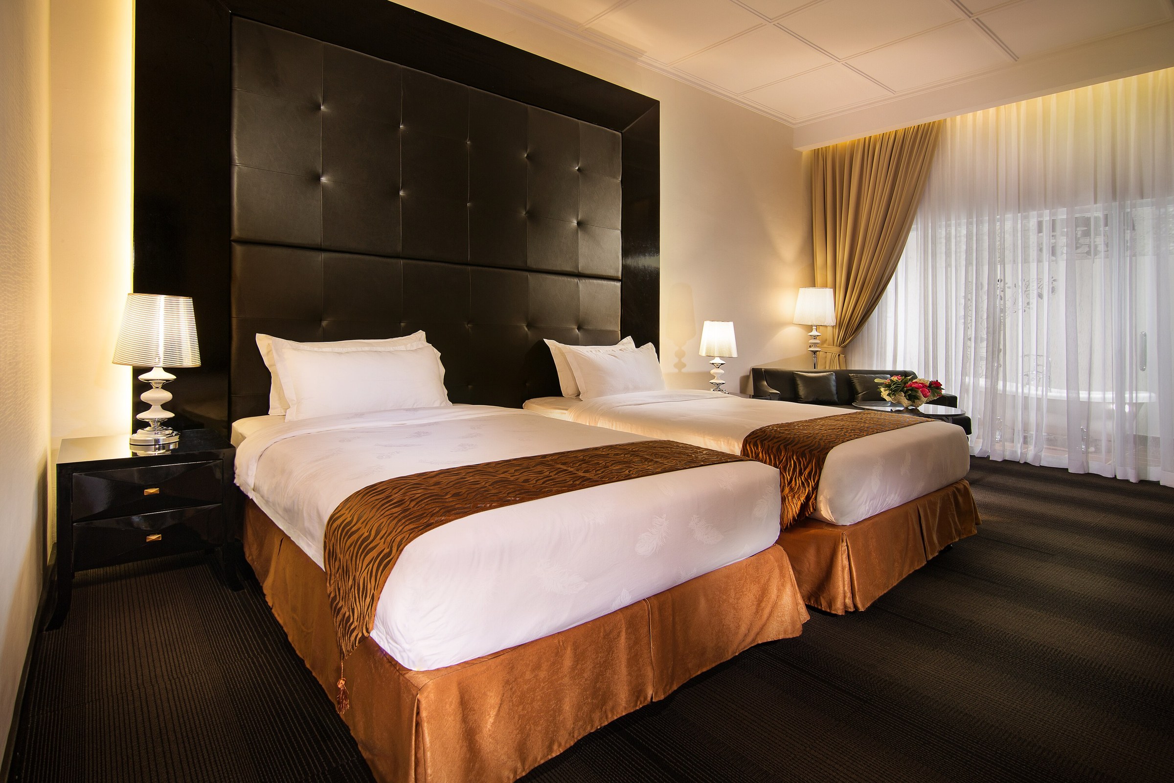 Two hotel beds with separate gold-brown tailored bed skirts and visible pleats beneath the white mattress bedding.
