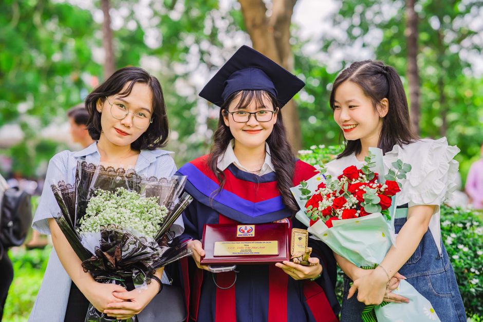 Three young women celebrating their graduation with smiles and bouquets.