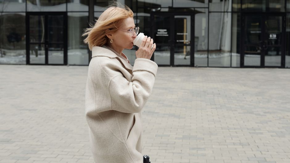 Confident businesswoman sipping coffee while walking outdoors. Stylish and professional lifestyle captured.