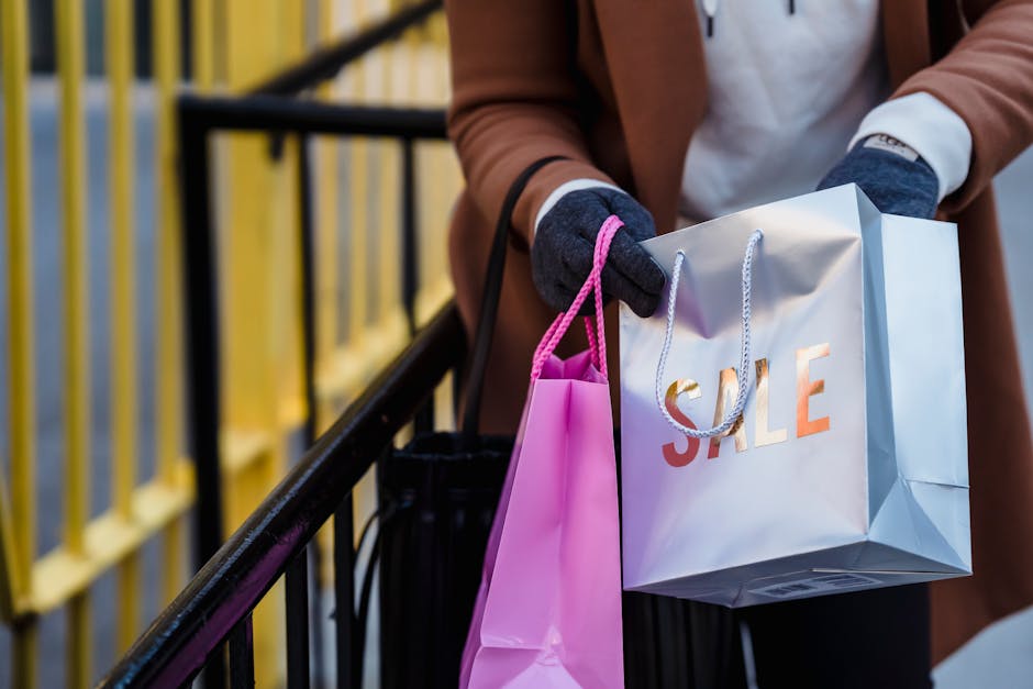 Crop anonymous female in warm coat and gloves looking in shopping bags with purchases while standing on city street on spring day