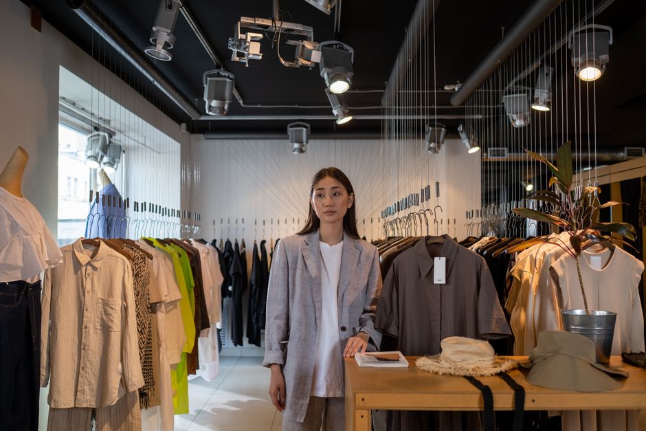 Stylish Asian woman standing in a modern clothing boutique, showcasing contemporary fashion.