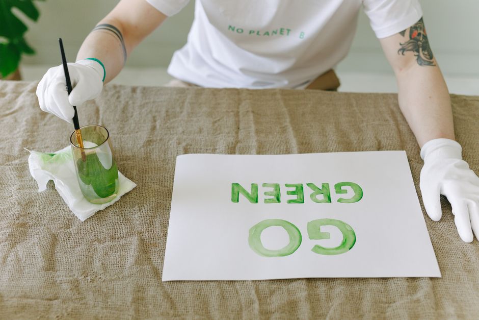 Person painting eco-friendly 'Go Green' message on paper with gloves and brush.