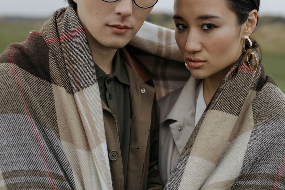 Elegant couple wrapped together in a plaid blanket, showcasing love and romance outdoors.