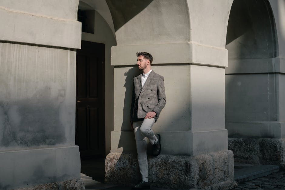 A fashionable man poses against arched architecture, capturing urban elegance.