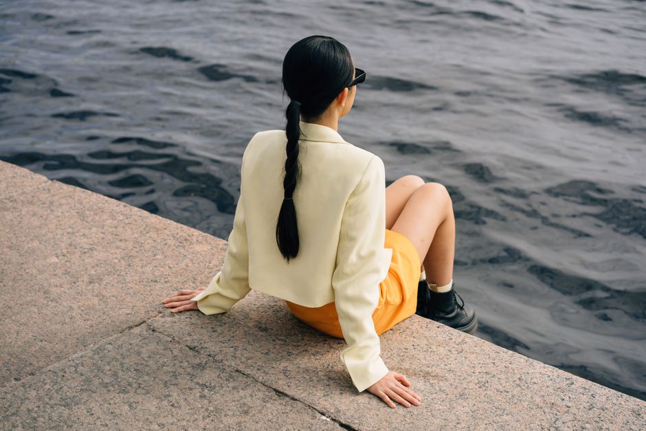 Woman in yellow attire sits by the seawall, enjoying the peaceful view.