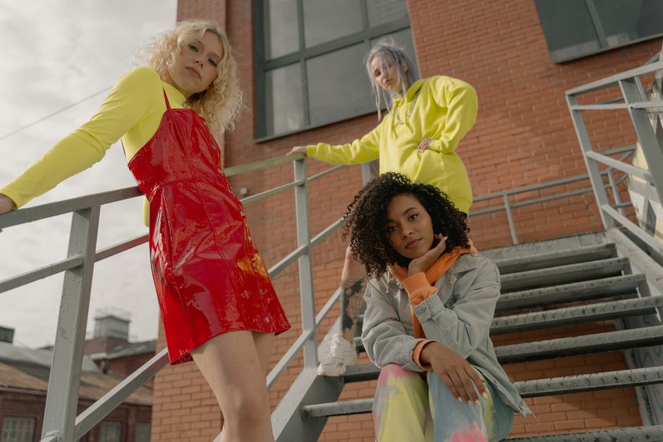Stylish women in colorful outfits posing on an outdoor staircase with an urban backdrop.