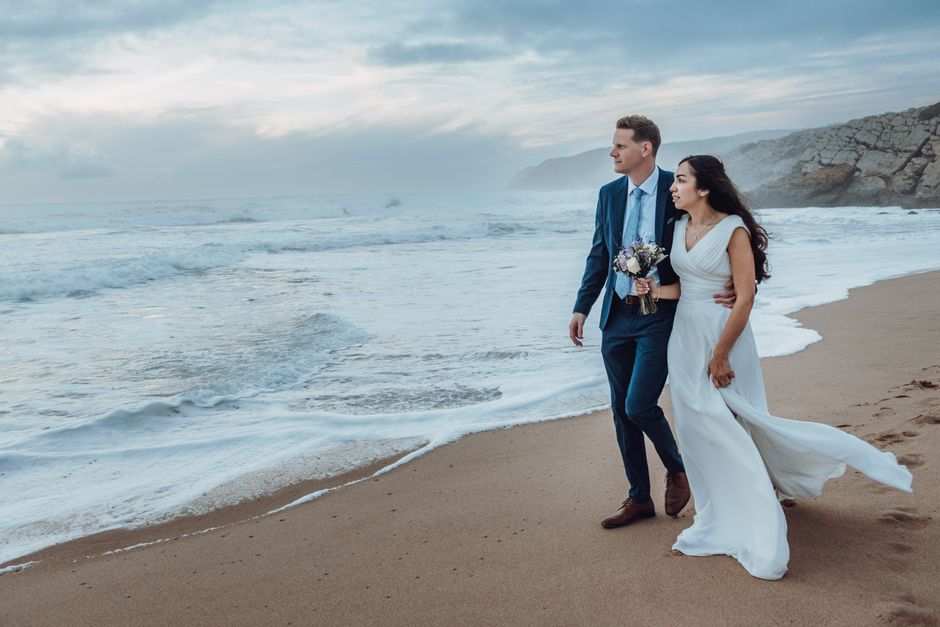 A couple in wedding attire strolls along a serene beach, capturing a moment of love and elegance by the sea.