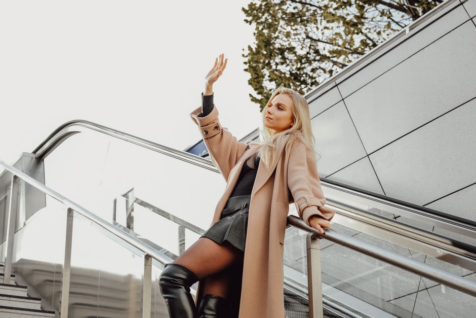Stylish woman in trench coat on an outdoor escalator, enjoying a sunny day.